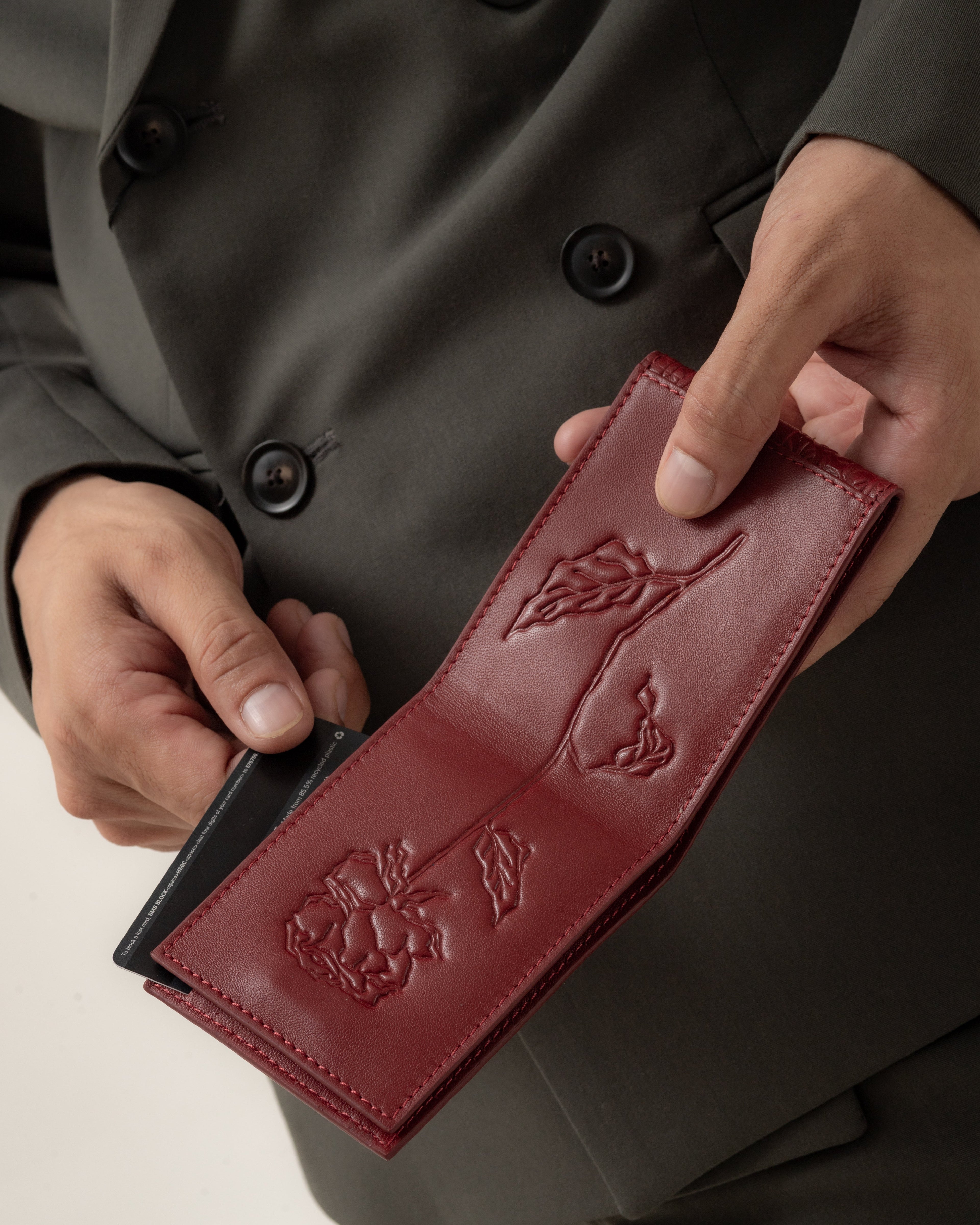 Person holding a red leather HB wallet with intricate designs, wearing a dark coat.